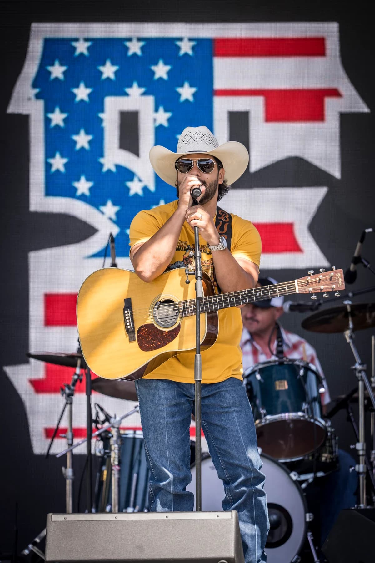 Buck Ford performing in a yellow shirt in front of an American flag
