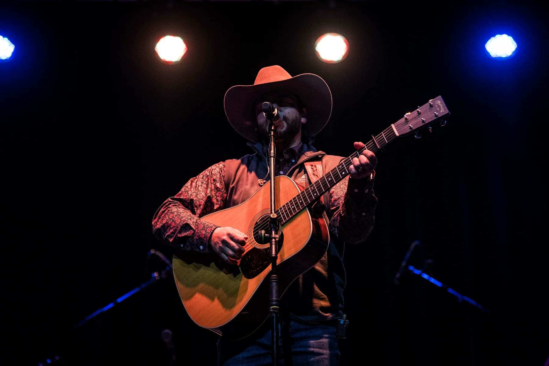 Buck Ford singing with his guitar under red stage lights