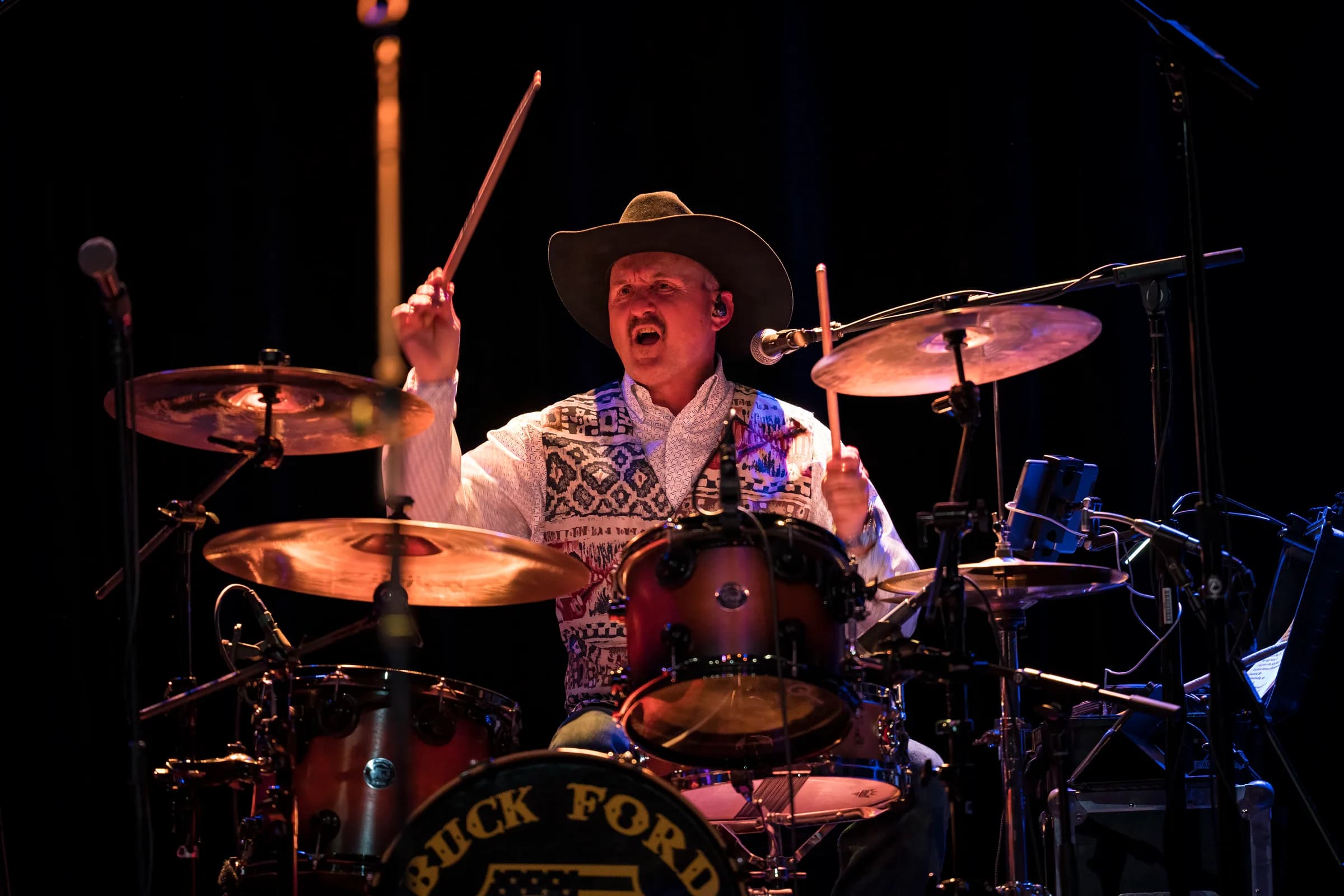 Drummer playing behind the kit beneath a warm spotlight