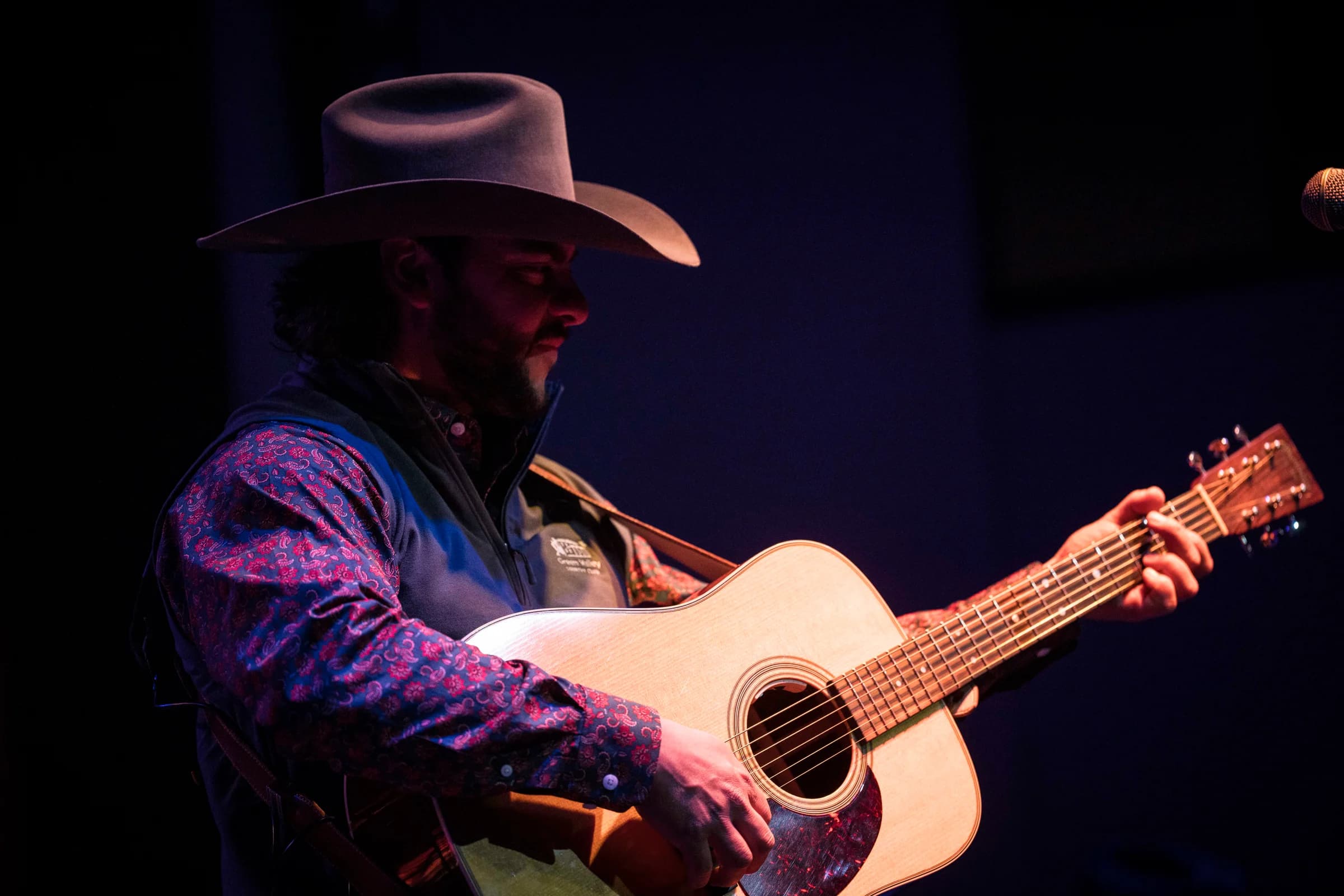 Buck Ford strumming his acoustic guitar in a close stage portrait