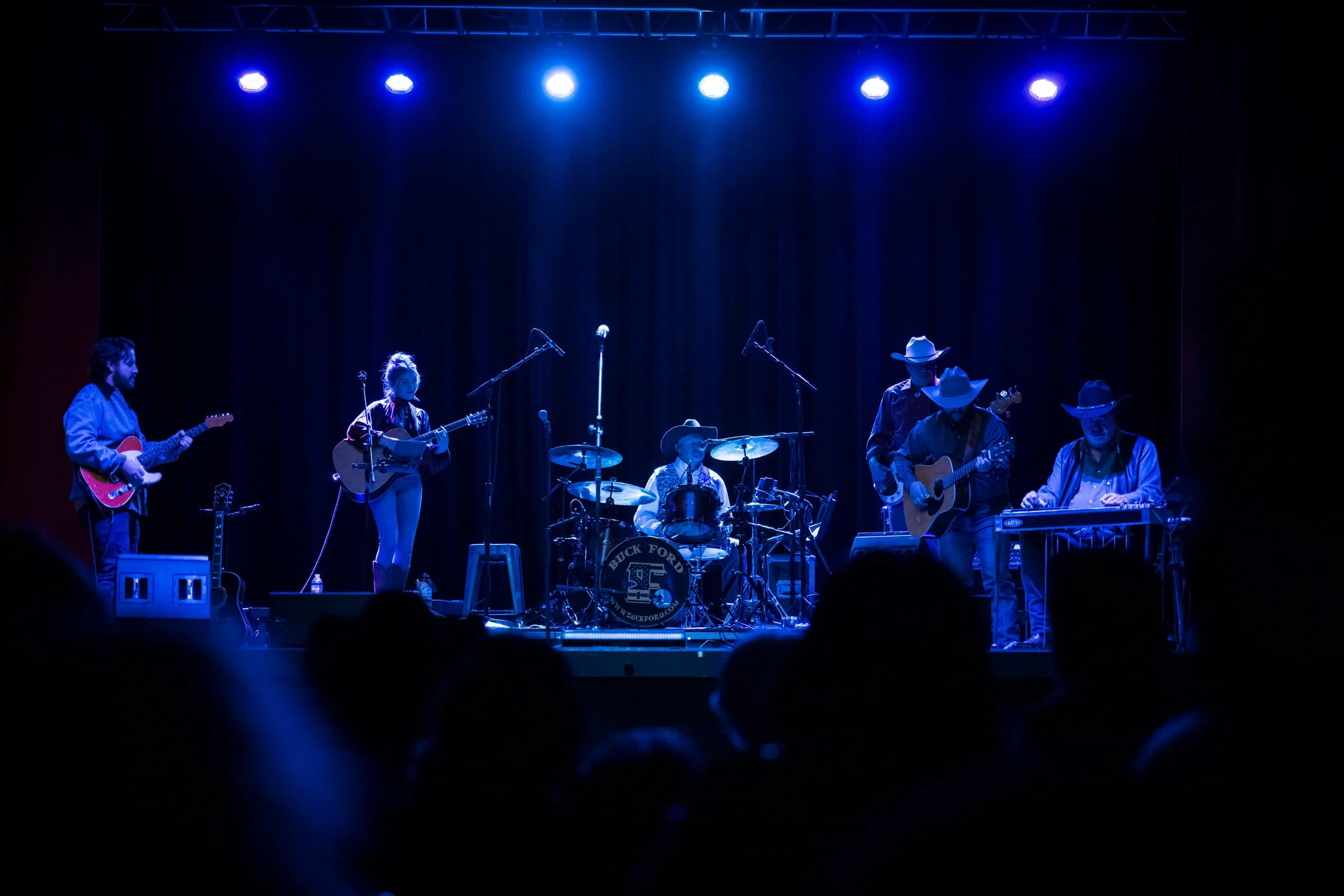 The full band performing beneath a row of blue spotlights