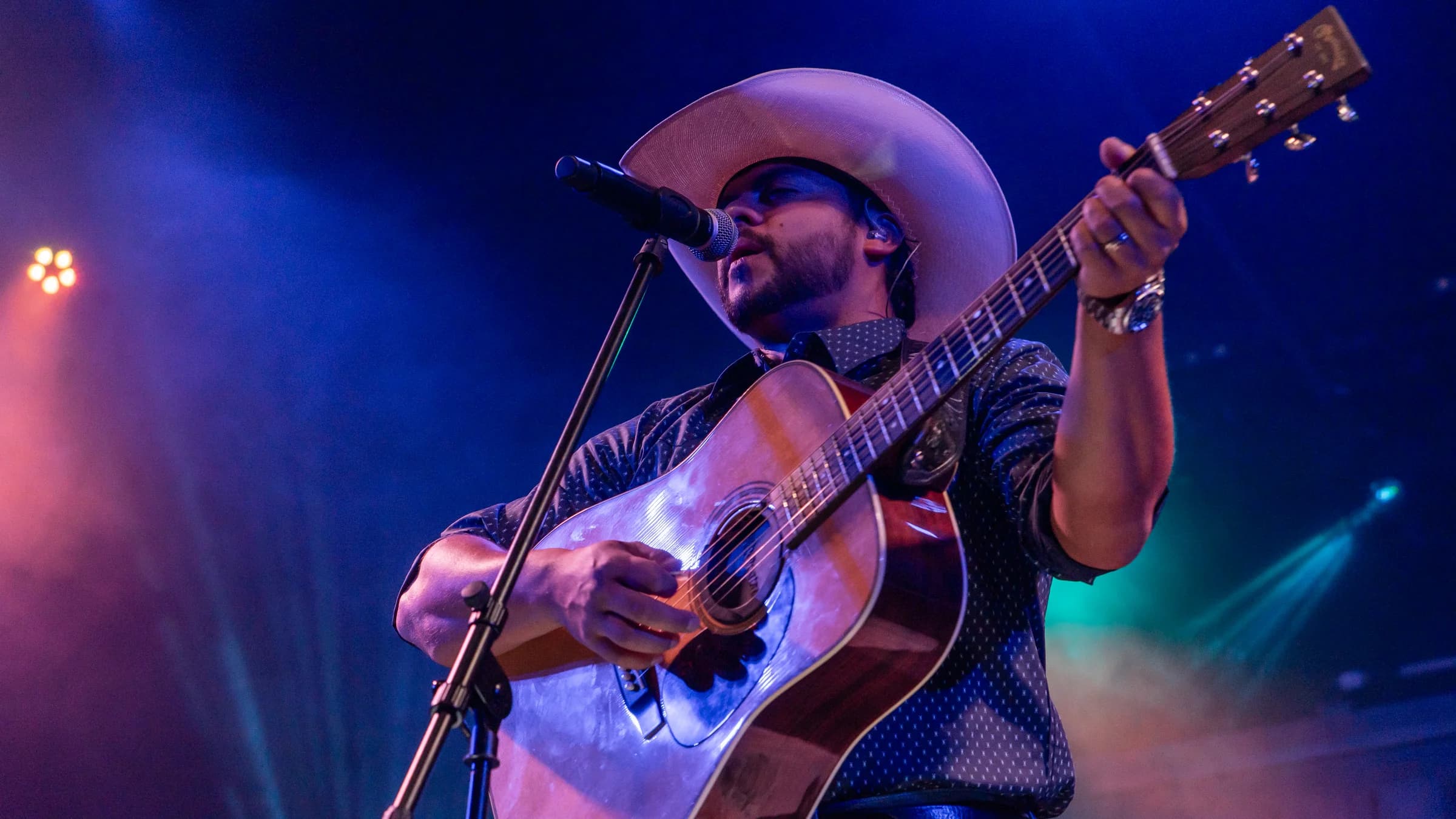 Buck Ford singing and playing acoustic guitar under blue stage lights